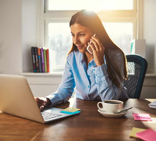 A professional woman working from a bright, organized desk, speaking on the phone while using her laptop—capturing the essence of Servcorp’s virtual office solutions