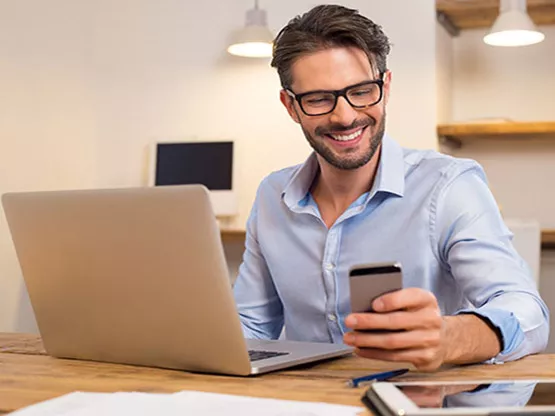 professional working remotely, using both his laptop and smartphone—perfectly representing the flexibility and connectivity offered by a virtual office at Servcorp.