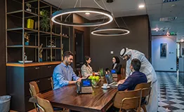 A group of professionals in a modern meeting room at Sahab Tower, Kuwait, engaged in discussion while enjoying a welcoming and well-serviced business environment.